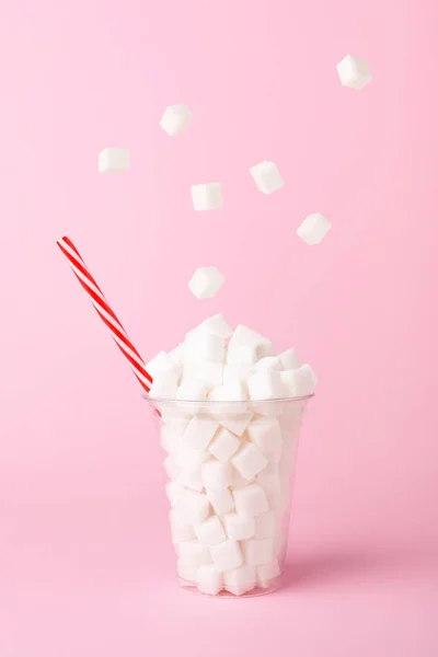 Gula batu jatuh ke dalam gelas pada latar belakang merah muda konsep pola makan tidak sehat — Stok Foto