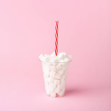 Pembe arka plan Sağlıksız gıda kavramı üzerinde saman dolu şeker küpleri ile Plastik fincan