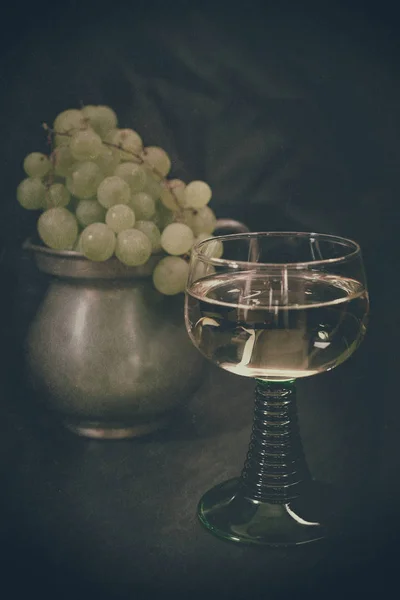 Ένα Ποτήρι Λευκό Κρασί Μπροστά Από Μια Μεταλλική Κανάτα Σταφύλια — Φωτογραφία Αρχείου