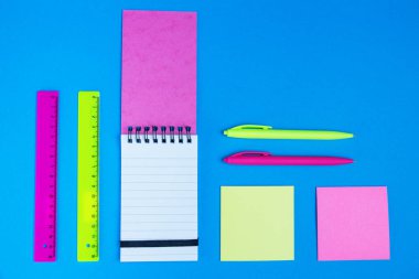 Pembe ve sarı neon Kırtasiye, kalem ve Cetveller, mesaj notlar ve Not defteri ışık mavi masa düz üzerinde yatıyordu