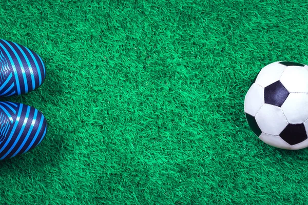 Soccer ball and cleats against green artificial turf
