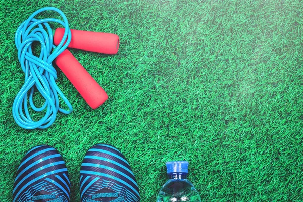 Skipping rope, trainers and water bottle against green artificial turf, top view with copy space, weight management and fitness concept