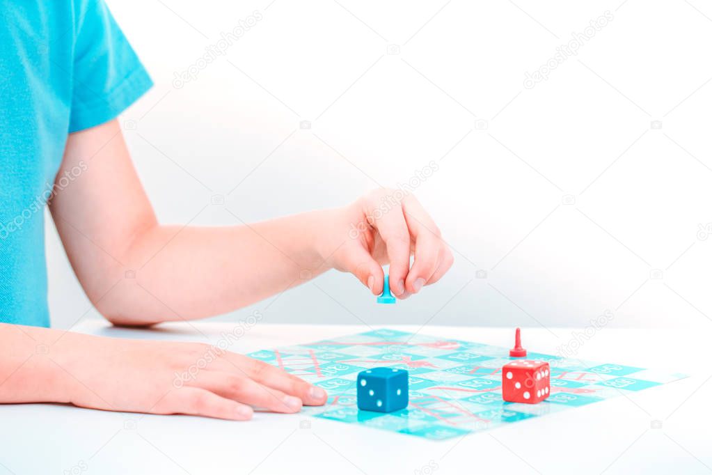 Child plays a board game snakes and ladders with colorful pieces and dice with both hands on tabletop. Copy space