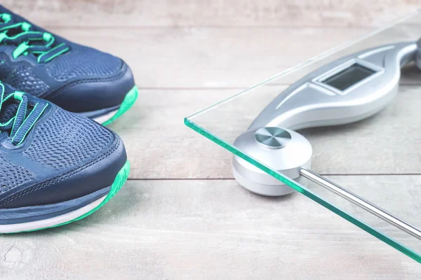 Running shoes and weighing scales on wooden surface
