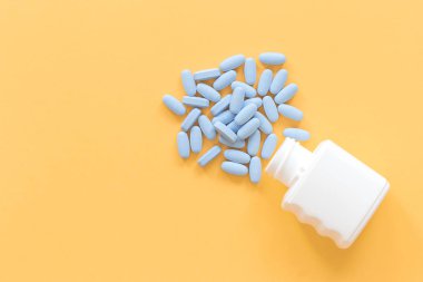 mavi tablet hapları sarı arka plan üzerinde konteyner düşen