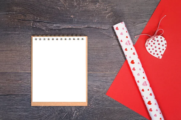 Heart and gift wrapping paper with notepad on wooden desk