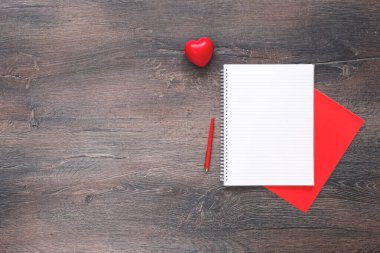 Ahşap masasında not defteri olan kırmızı bir kalp.