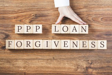 Kaba dokulu arka planda tahta bloklar üzerine PPP LOAN Af metni. Kadın eli engelleri tutuyor. Küçük işletme maaş koruma programı. Bankacılık ve finans kavramı