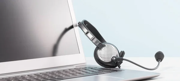 Masa mavi arka planında kulaklık olan boş ekranlı bir dizüstü bilgisayar parçası. kopyalama alanı. Uzaktan öğrenme ya da evden çalışma, çevrimiçi kurslar ya da alışveriş asgari konsept. Yardım masası veya çağrı merkezi kulaklığı