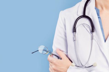 Kadın doktor göz doktoru veya göz doktoru ince metal çerçeveli bir çift gözlük tutuyor. Minimum afiş, mavi arka plan. Uzayı kopyala Göz doktoru, göz muayenesi. Tıp modelleme şablonu