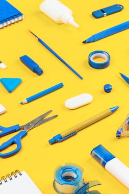Parlak sarı arka planda çeşitli ofis ve okul beyaz ve mavi kırtasiye malzemeleri. Okula dönmek ya da eğitim ve zanaat konsepti için örgütlenmiş. Seçici odak