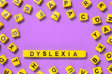 Disleksi kelimesi pembe mor üzerine sarı, etrafa dağılmış harf küpleri, okuma zorluğu ve düzensizlik görsel ve işitsel hafıza veya test konsepti. Kopyalama alanı olan eğitim ve nöroloji