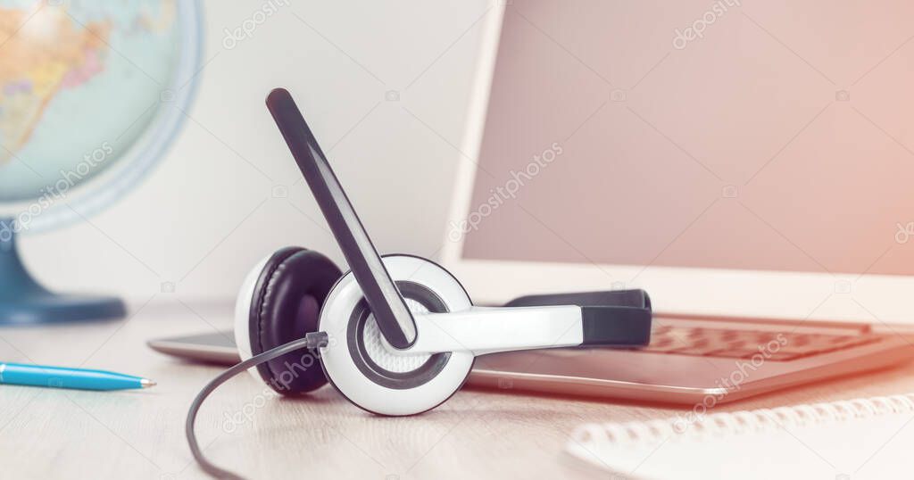 Laptop with blank screen and headphones on white desk blue background world globe. Distant learning or working from home, online courses or travel agent concept. Helpdesk or call center headset banner