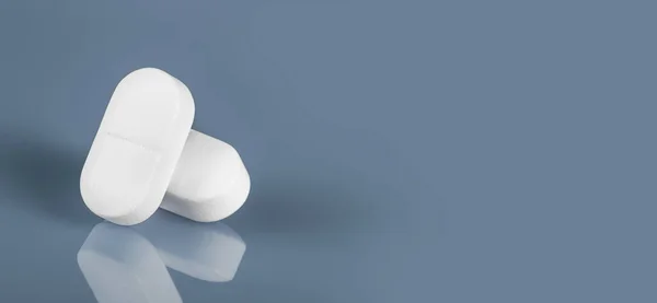 Mavi bardağa yansıyan iki beyaz tablet ya da hap. Boşluğu kopyala. Görüntü afişini kapat. İlaç güvenli tüketim ve tedavi, aşı ve aşılama. İlaç, sağlık ve eczane konsepti