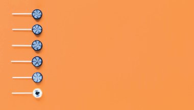 Mutlu Cadılar Bayramı sıra Örümcek Ağı lolipop şekerlemeleri ve turuncu arka planda farklı bir tane. Fotokopi alanı olan düz bir pankart. Şaka mı şeker mi?