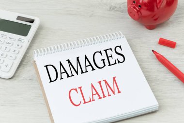 Hasarlar not defterinde yazılı. Hesap makinesi ve kırmızı para bankası olan ofis masası. İş sigortası, kişisel hak talebi.