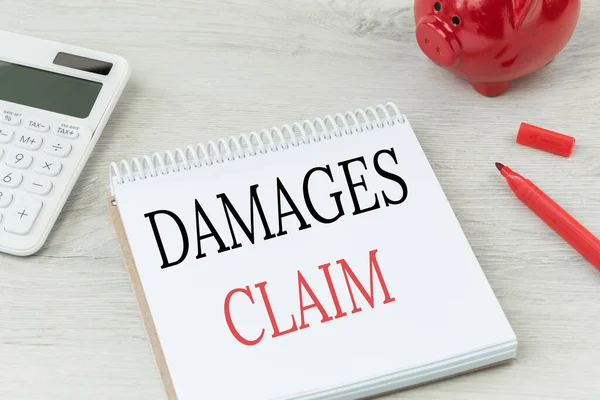 Hasarlar not defterinde yazılı. Hesap makinesi ve kırmızı para bankası olan ofis masası. İş sigortası, kişisel hak talebi.