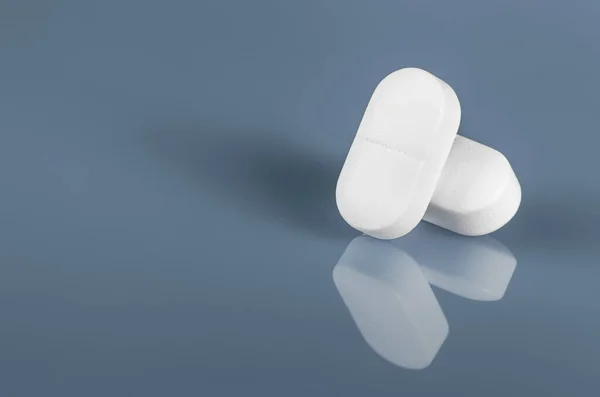 Mavi bardağa yansıyan iki beyaz tablet ya da hap. Alan yakın görüntüsünü kopyala. İlaç güvenli tüketim ve tedavi, aşı ve aşılama. İlaç, sağlık ve eczane konsepti