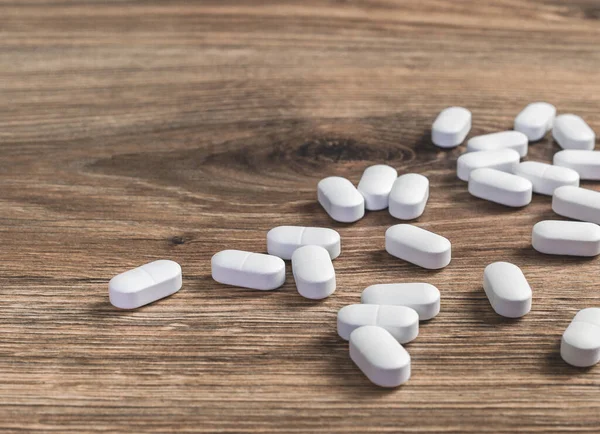 医学的背景 木製のテーブルの上に散在するいくつかの白いカプセル錠や錠剤 ヘルスケア薬局と医療の概念 鎮痛剤や処方薬の消費 スペースのコピー — ストック写真