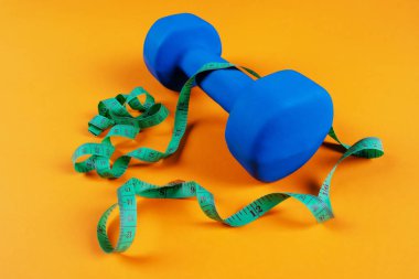 Bir mavi dumbbell ve turuncu arka plan üzerinde ölçüm bandı