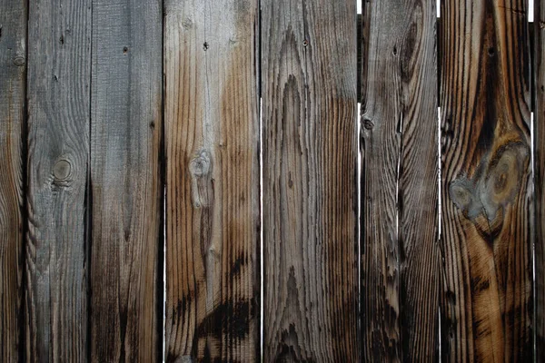 Old grey fence made of many wooden planks which are slightly burnt and scratched as a background.