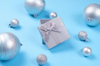Güzel açık gümüş hediye kutusu parlak Noel baubles mavi pastel arka plan ve sevimli ipeksi yayla bileşimi. Noel ve yeni yıl kutlama kavramı.