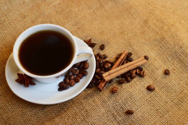 Siyah beyaz porselen fincan kahve fasulye, tarçın ve Yıldız anason çuval bezi zemin üzerine aromalı. Seçici odak.