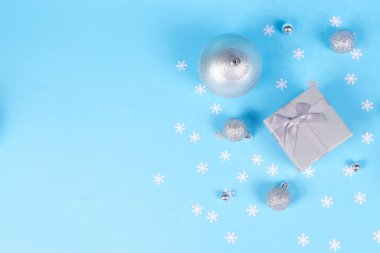 Kar tanesi konfeti kopya alanı ile kompozisyon güzel gümüş hediye kutusu şirin ipeksi yay ve mavi arka plan üzerinde irili ufaklı parlak Noel baubles ile süslenmiş.