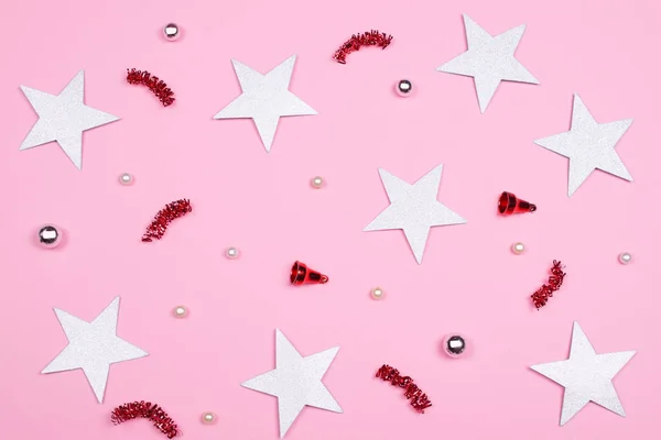 Festive pink background of red and silver shiny beads, glitter stars, red decorative bells and confetti. Celebration concept.