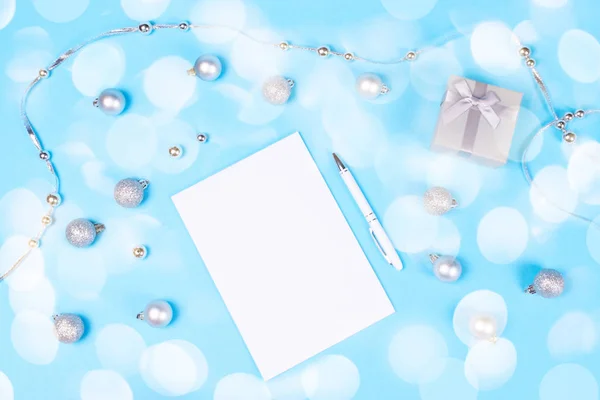 假日装饰配件的圣诞小球和珠子 可爱的银礼品盒 笔记本和笔写在柔和的蓝色背景照亮与节日的灯光创造大气的心情 — 图库照片