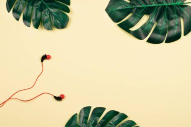 Üç güzel parlak ve satureted yapay monstera palmiye yaprakları ve pastel sarı zemin üzerine kırmızı vakum kulaklık. Zarif dekorasyon öğeleri. Metin için yer kopyalayın. Yaz saati ve yaşam tarzı. Doğa kavramı için dinleme.