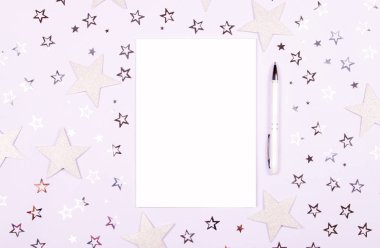 Defter ile boş sayfa ve kalem beyaz masada dekore ile parlak ve konfeti yıldızlı glitter. Parlak ve şenlikli zemin. Minimalist tebrik kavramı. Kopya alanı ile üstten görünüm.