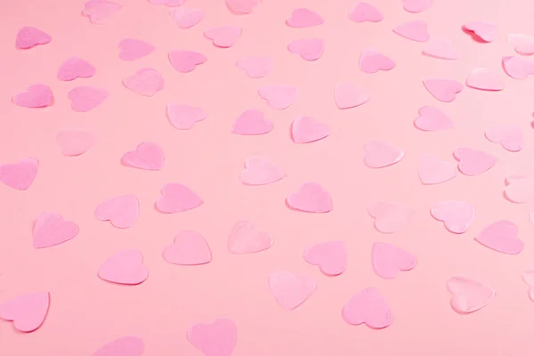 Pastel pink background with scattered heart-shaped confetti of the same color with copy space for text. Valentine\'s Day concept. Love symbols. Festive backdrop.