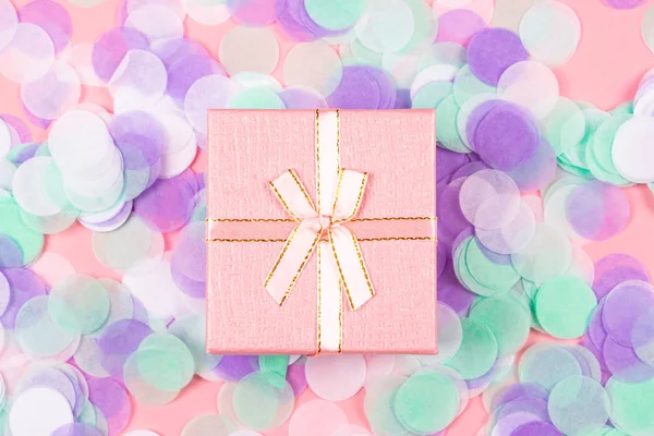 Present box on pink background with multicolored confetti.