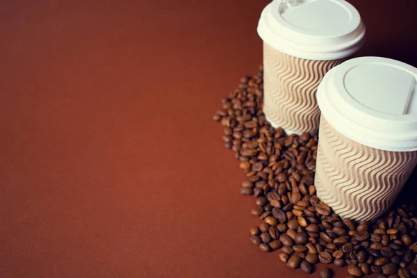 Két papír csésze kávé és a bab, barna háttér. — Stock Fotó