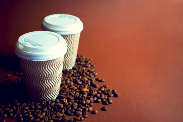 Две бумажные чашки кофе и бобы на коричневом фоне . — стоковое фото