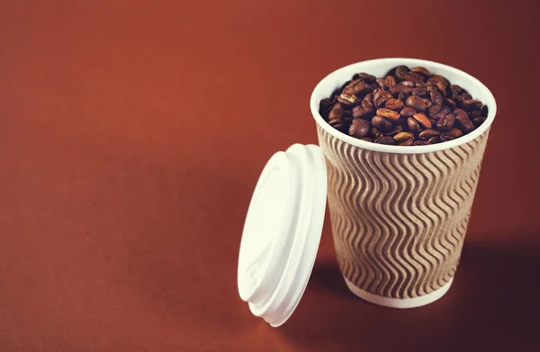 Бумажная чашка кофе и бобы на коричневом фоне . — стоковое фото