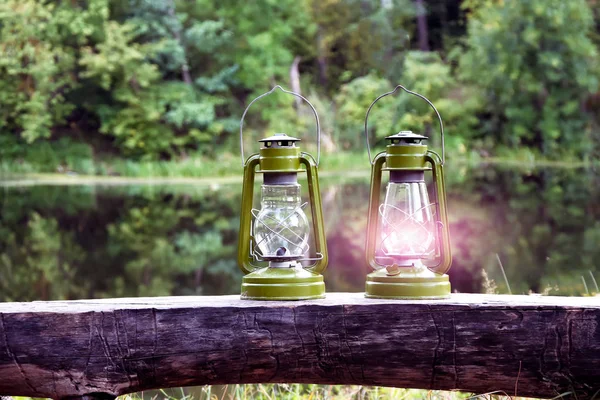 Two kerosene lamps. An ancient oil lamp burns fairy forest against the background of the river. Symbol love romance in rustic style