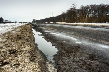 yol çukurları ve kar üzerinden su birikintileri çatlaklar ile kaplıdır. Yatay gri bulutlu havalarda kış yolun. Yol onarım kavramı, arabanın sürücüsü için opaklık