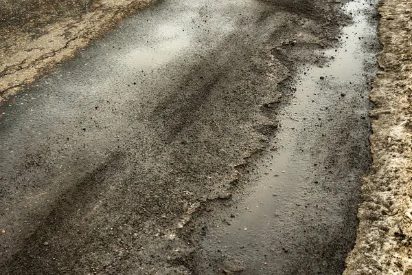 road is paved with cracks in pits and puddles from the snow. Landscape of the winter road in cloudy gray weather. Concept of road repair, opacity for the driver of the car