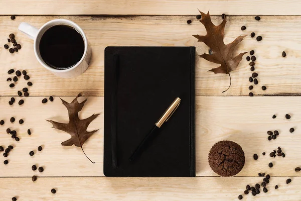 Working concept. Diary with pen, cup of coffee and muffin on a wooden board with a coffee bean frame. Top view.