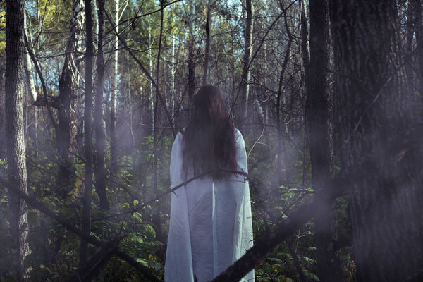 Portrait of a dead girl on Halloween in a gloomy forest. A ghost-girl in a gloomy dark forest at night on Halloween
