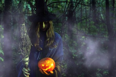 Genç karanlık ormanda Cadılar Bayramı'nda cadı. Kız kılığında bir cadıyla Jack-o-lantern puslu bir ormanda geceleri.