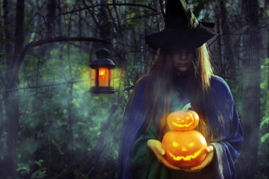 Genç karanlık ormanda Cadılar Bayramı'nda cadı. Kız kılığında bir cadıyla Jack-o-lantern puslu bir ormanda geceleri.