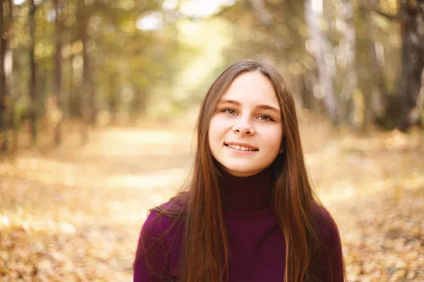 Charming girl in the autumn forest. Portrait of a teenager in autumn park on sunny day.