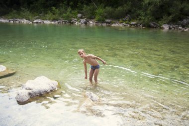 Çocuk nehirde duruyor ve etrafa su sıçrıyor.