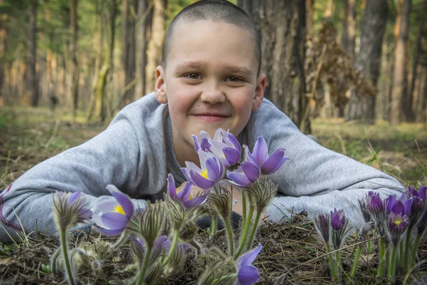 In de bos jongen ligt op de grond en knuffels de bloemen naar PA — Stockfoto