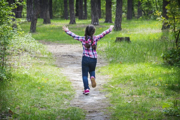 In de zomer, op een heldere zonnige dag in het bos, een klein gelukkig meisje loopt langs het pad. — Stockfoto