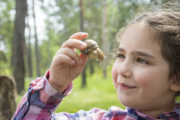 In de zomer in het bos onderzoekt een klein meisje een slak. — Stockfoto