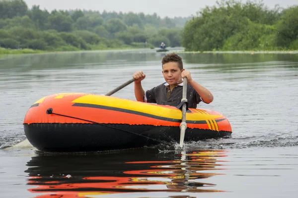In summer, the boy floats on the river in an inflatable boat. He — Stock Photo, Image